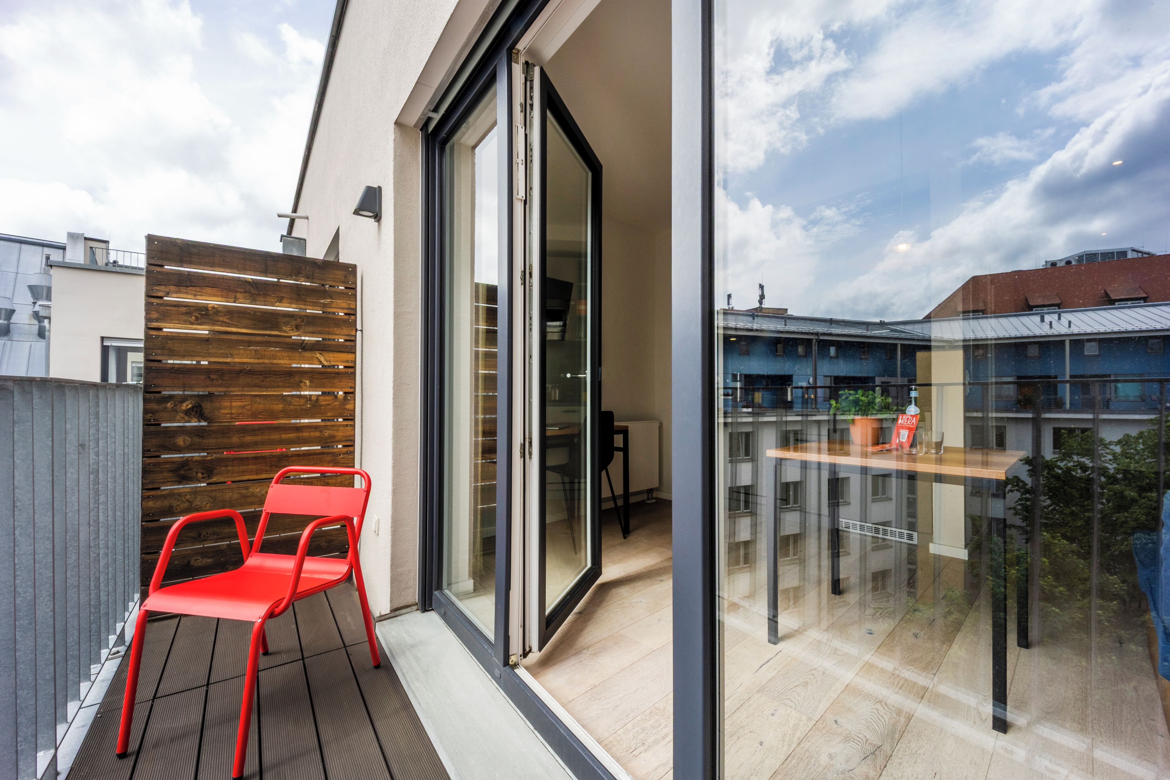 Ein moderner Balkon mit einer Schiebeglastür, einem roten Stuhl und einer Wand aus Holzlatten.