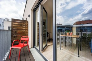 A modern balcony with a sliding glass door, a red chair, and a wooden slatted wall. - Brera Serviced Apartments Leipzig (Leipzig)