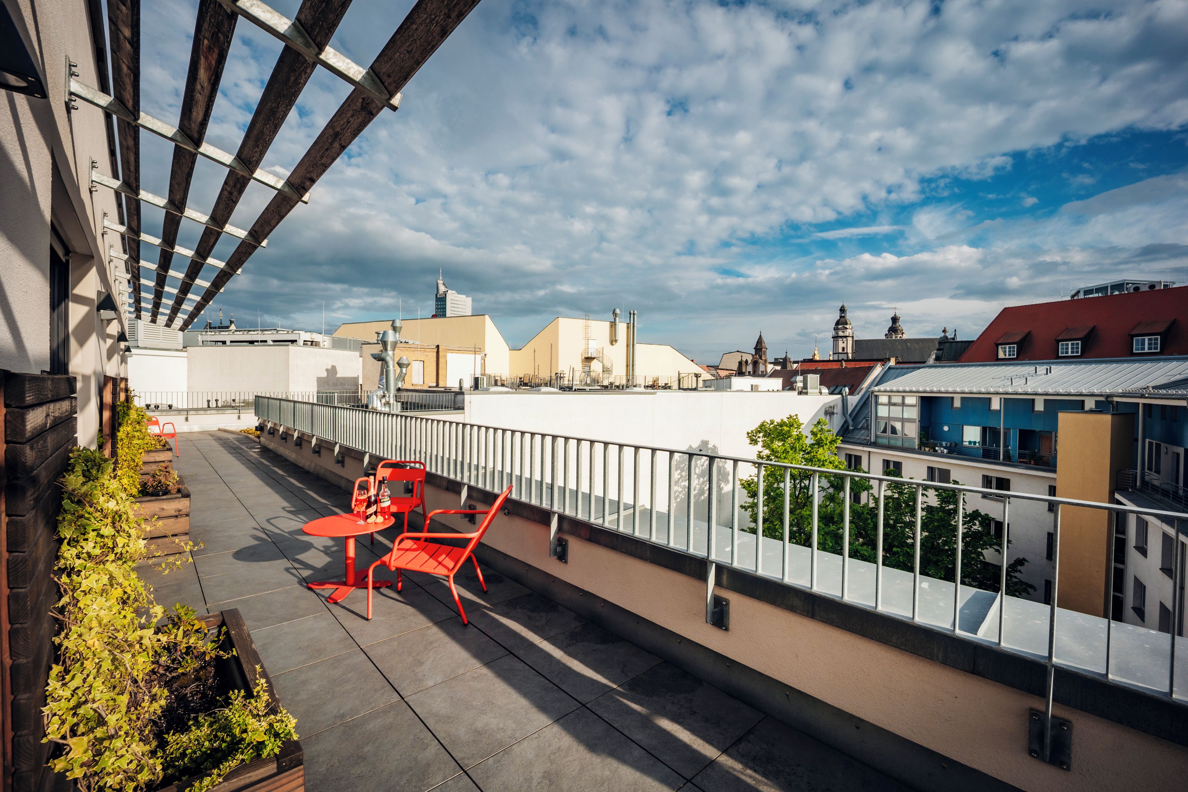 Eine Dachterrasse mit Tisch und Stühlen, mit Blick auf eine Stadtlandschaft und verschiedene Gebäude.