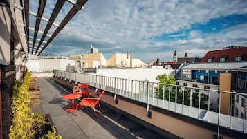 A rooftop terrace with a table and chairs, overlooking a cityscape with various buildings.