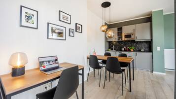 A modern kitchen with a dining area, featuring a laptop on a table, framed pictures on the wall, and pendant lighting.