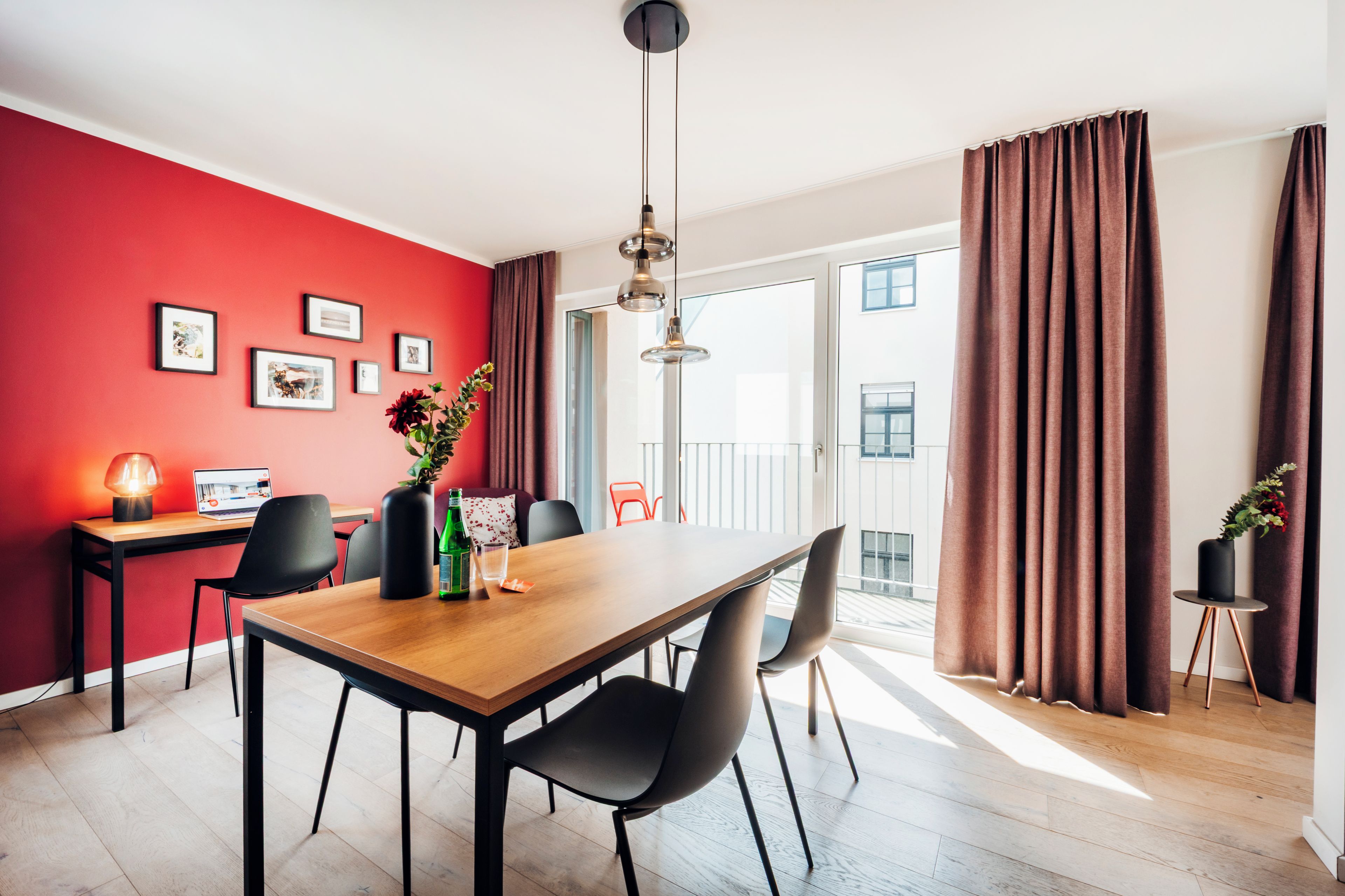 Ein moderner Essbereich mit einem Holztisch, schwarzen Stühlen, einem Laptop und einer Blumenvase.