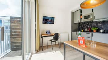 A modern kitchen with a dining area, a TV mounted on the wall, and a balcony with a view.