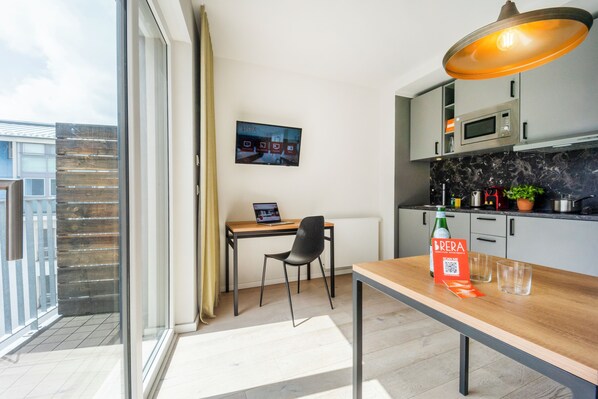 A modern kitchen with a dining area, a TV mounted on the wall, and a balcony with a view. - Brera Serviced Apartments Leipzig (Leipzig)