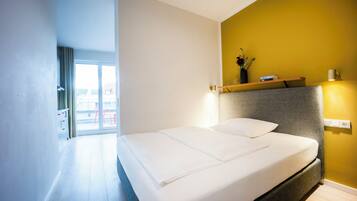 Une chambre d’hôtel moderne avec un grand lit, une vue sur l’extérieur et un mur d’accent jaune.