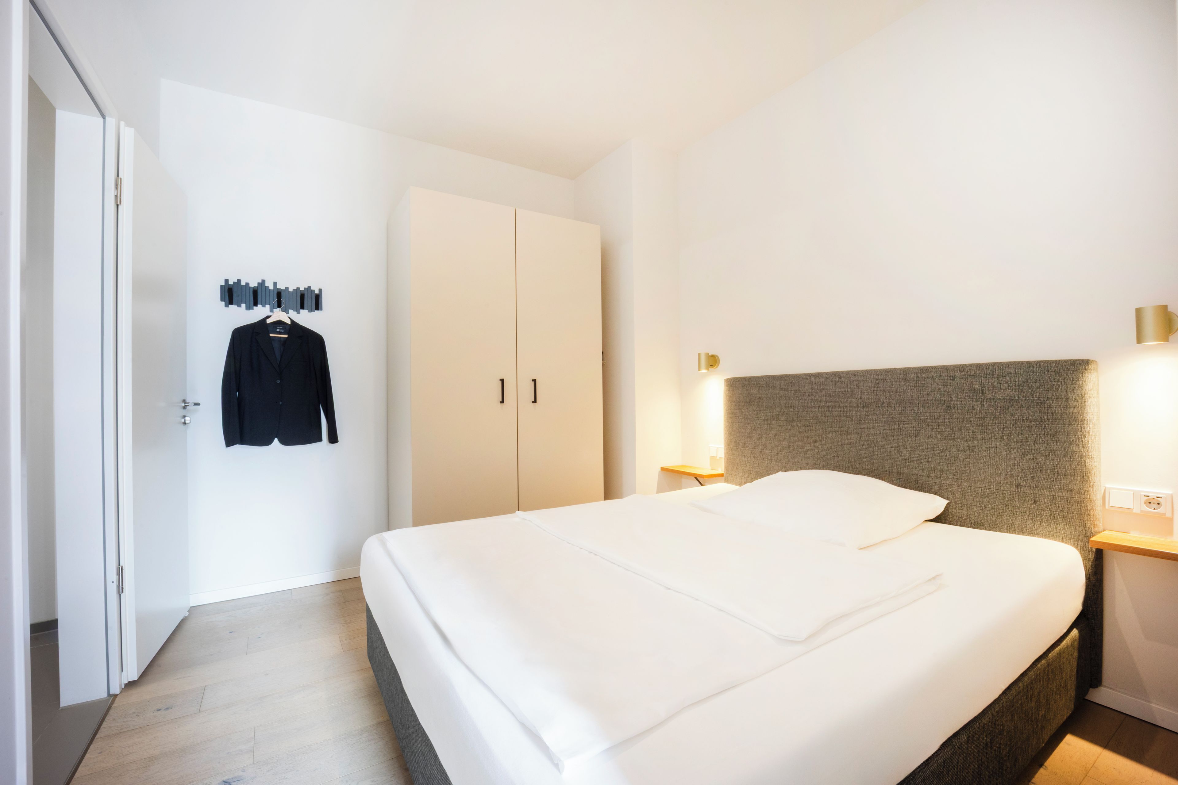 Ein Hotelzimmer mit Bett, Schrank, Kleiderhaken und Nachttisch mit Lampe.