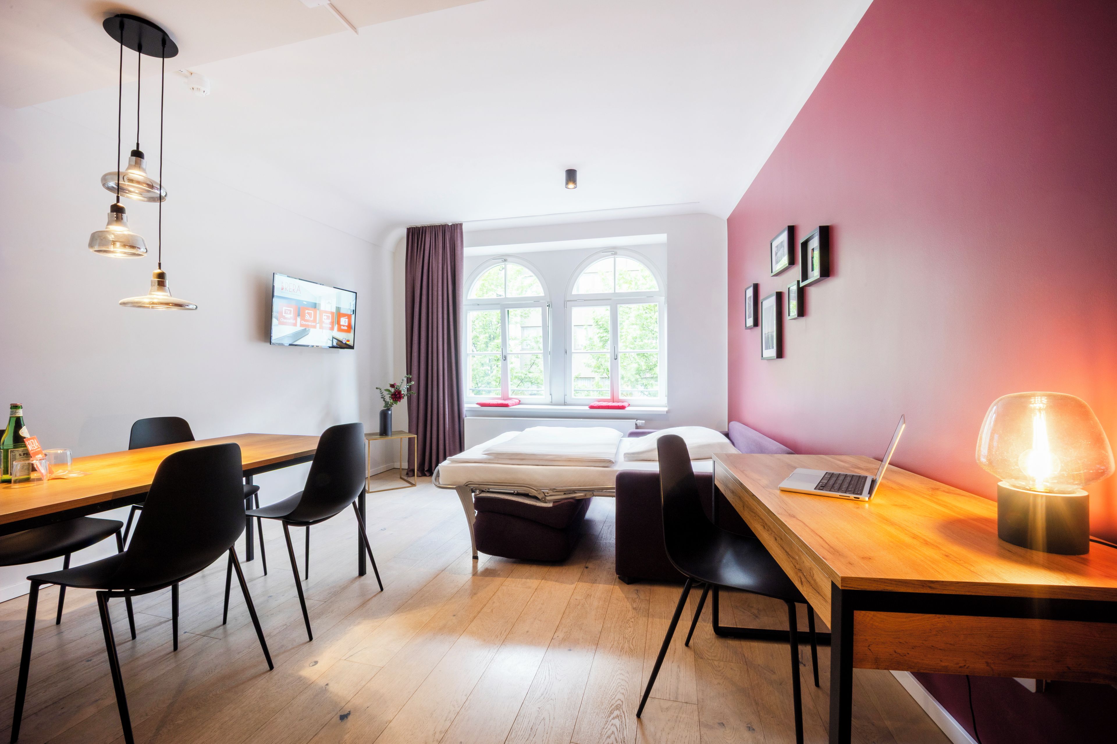 A modern room with a wooden desk, black chairs, a bed, a window with curtains, and a laptop on the desk.