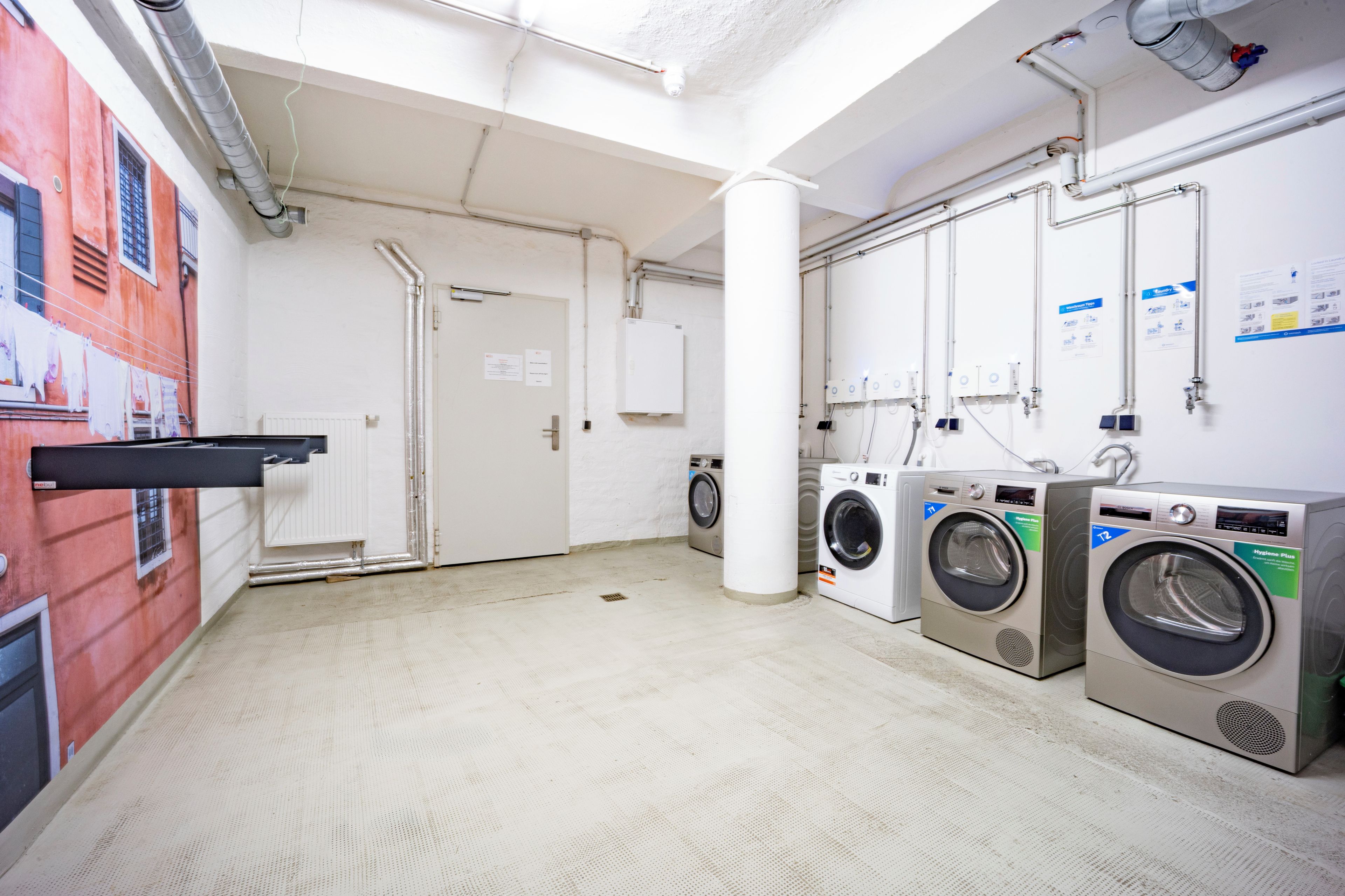 A laundry facility with multiple washing machines, a drying rack, and a white door.