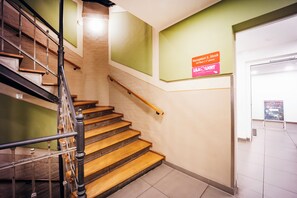 Una escalera con escalones de madera y barandillas de metal, que conduce a una puerta con un letrero que indica recepción en el primer piso.