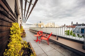 A rooftop terrace with a wooden wall, a metal railing, and a view of city buildings. - Brera Serviced Apartments Leipzig (Leipzig)