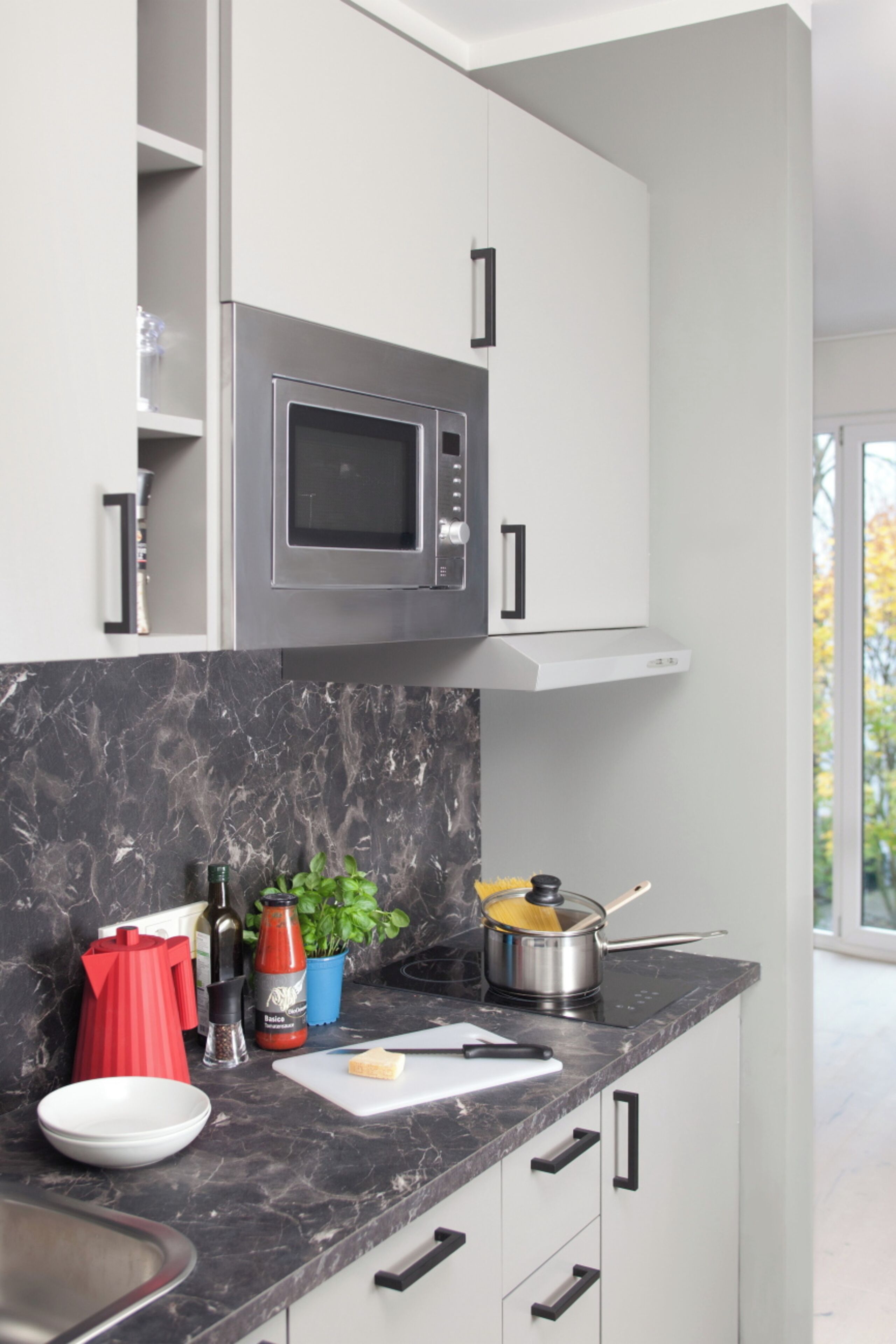 A modern kitchen with a built-in microwave, a marble countertop, and a window providing a view of the outdoors.