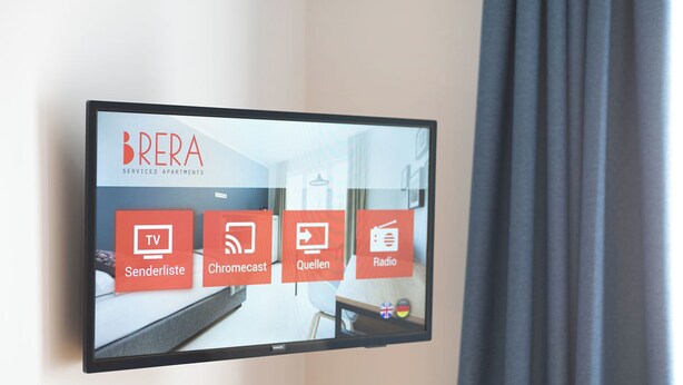 Pantalla digital en una habitación de hotel que anuncia apartamentos con servicios BRERA, con comodidades como TV, Senderliste, Chromecast, Quellen y Radio.