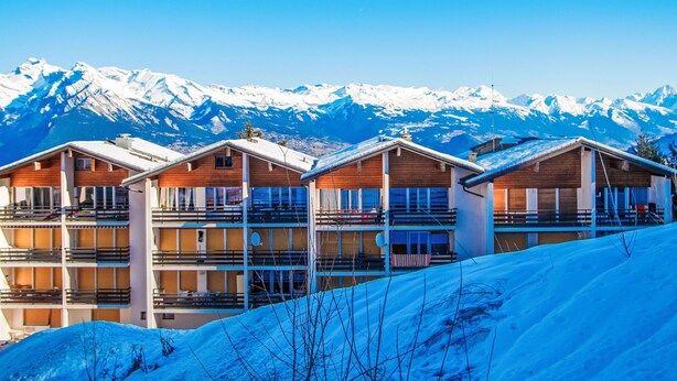 Une rangée de chalets en bois dotés de balcons, se dressant sur un fond de montagnes enneigées.