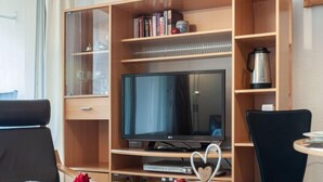 Une chambre d’hôtel moderne équipée d’une télévision, d’une bibliothèque, d’une machine à café et d’une petite table ronde agrémentée d’un décor en forme de cœur.