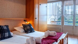 Une chambre d’hôtel avec deux lits, une armoire en bois, de grandes fenêtres et une vue sur l’extérieur.