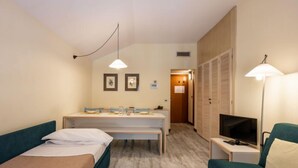 Een hotelkamer met twee eenpersoonsbedden, een bureau met stoel, een televisie en een kledingkast.