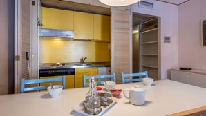Een moderne keuken met gele kastjes, een roestvrijstalen afzuigkap en een eethoek met een witte tafel gedekt voor twee personen.