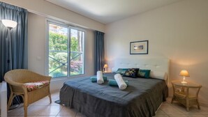 A bedroom with a large bed, a chair, a bedside table, and a window with curtains. - Eden Cap by Interhome (Antibes)
