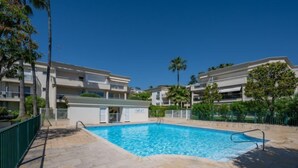 A swimming pool surrounded by multi-story buildings with balconies, a clear sky, and palm trees. - Eden Cap by Interhome (Antibes)