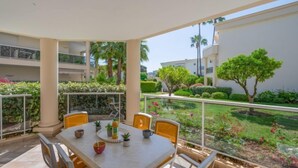 A covered outdoor dining area with a table and chairs, surrounded by greenery and a view of other buildings. - Eden Cap by Interhome (Antibes)
