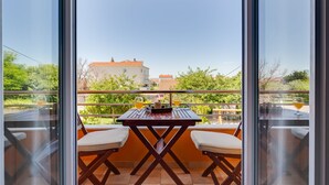 Un balcon avec une table et deux chaises, donnant sur un quartier résidentiel bordé d’arbres et de maisons.