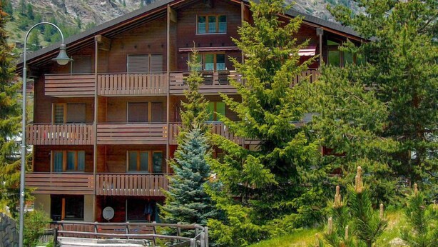 A multi-story wooden building with balconies, surrounded by trees and mountains. - Sungold by Interhome (Zermatt)
