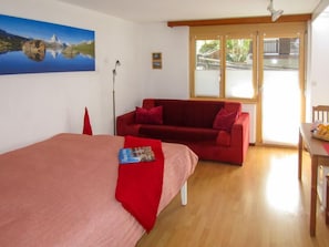 A room with a bed, a red sofa, a table with fruit, and a painting on the wall.