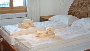 A double bed with neatly folded towels, a wooden headboard, and a window with curtains. - Residenza Chesa Margun 66-2 by Interhome (Silvaplana-Surlej)