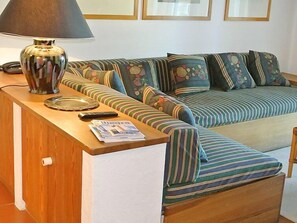 Een gezellige zithoek met een bank, een lamp en een kleine tafel met een afstandsbediening en kranten.