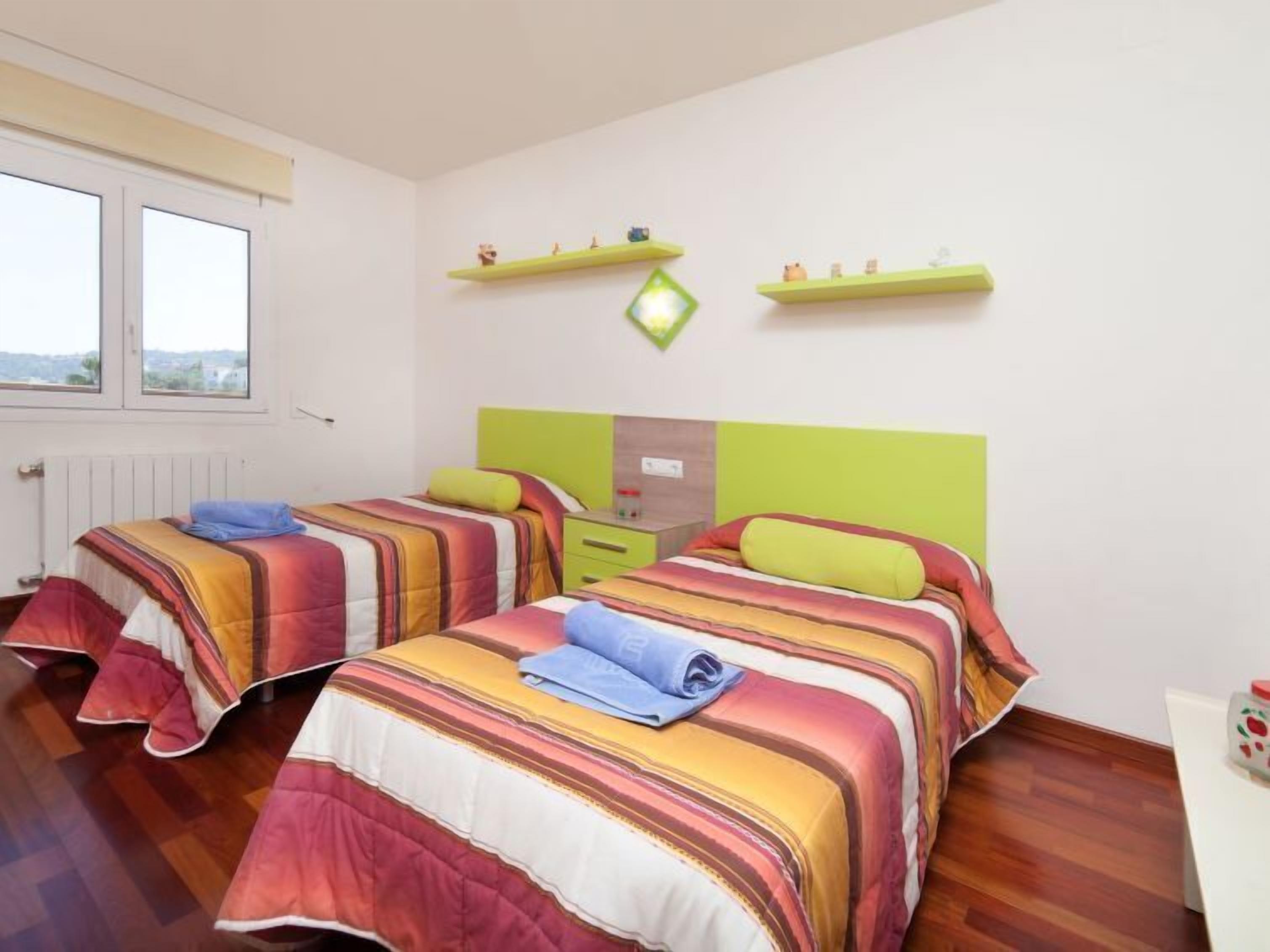 Une chambre avec deux lits, chacun étant équipé de draps à rayures, une fenêtre et un radiateur.