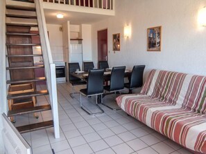 A modern living room with a striped sofa, a dining table with chairs, and a staircase.
