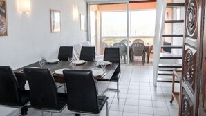 A dining area with a long table, black chairs, and a view of the outdoors through large windows.
