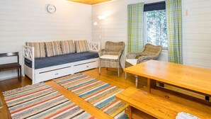 A cozy room with a wooden ceiling, a white wall, a sofa with striped cushions, two wicker chairs, a wooden table, and a colorful striped rug. - Piilopirtti by Interhome (Kaavi)