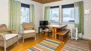 A cozy room with a wooden ceiling, two wicker chairs, a wooden table, a television, and a view of a snowy landscape through large windows. - Piilopirtti by Interhome (Kaavi)