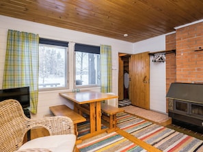 A cozy room with a wooden ceiling, a fireplace, a dining table with benches, and a television.