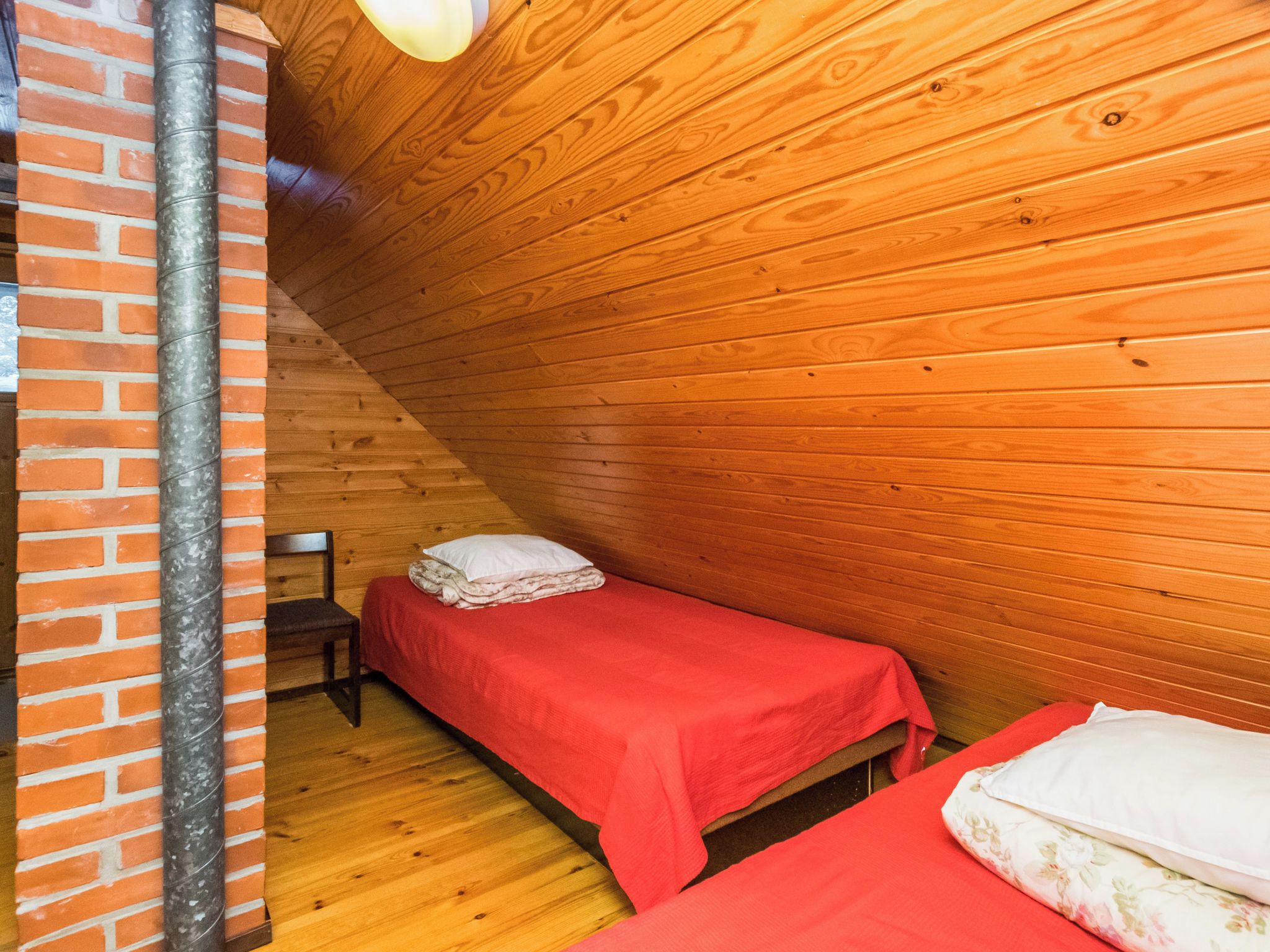Una habitación pequeña y acogedora con paredes de madera y techo inclinado, con dos camas individuales y una pared de ladrillo.