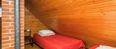 Una stanza accogliente e piccola con pareti in legno e soffitto spiovente, arredata con due letti singoli e una parete in mattoni.
