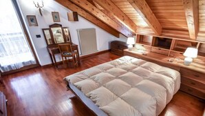 Een slaapkamer met een houten plafond, een groot bed, een dressoir, een stoel en een spiegel.