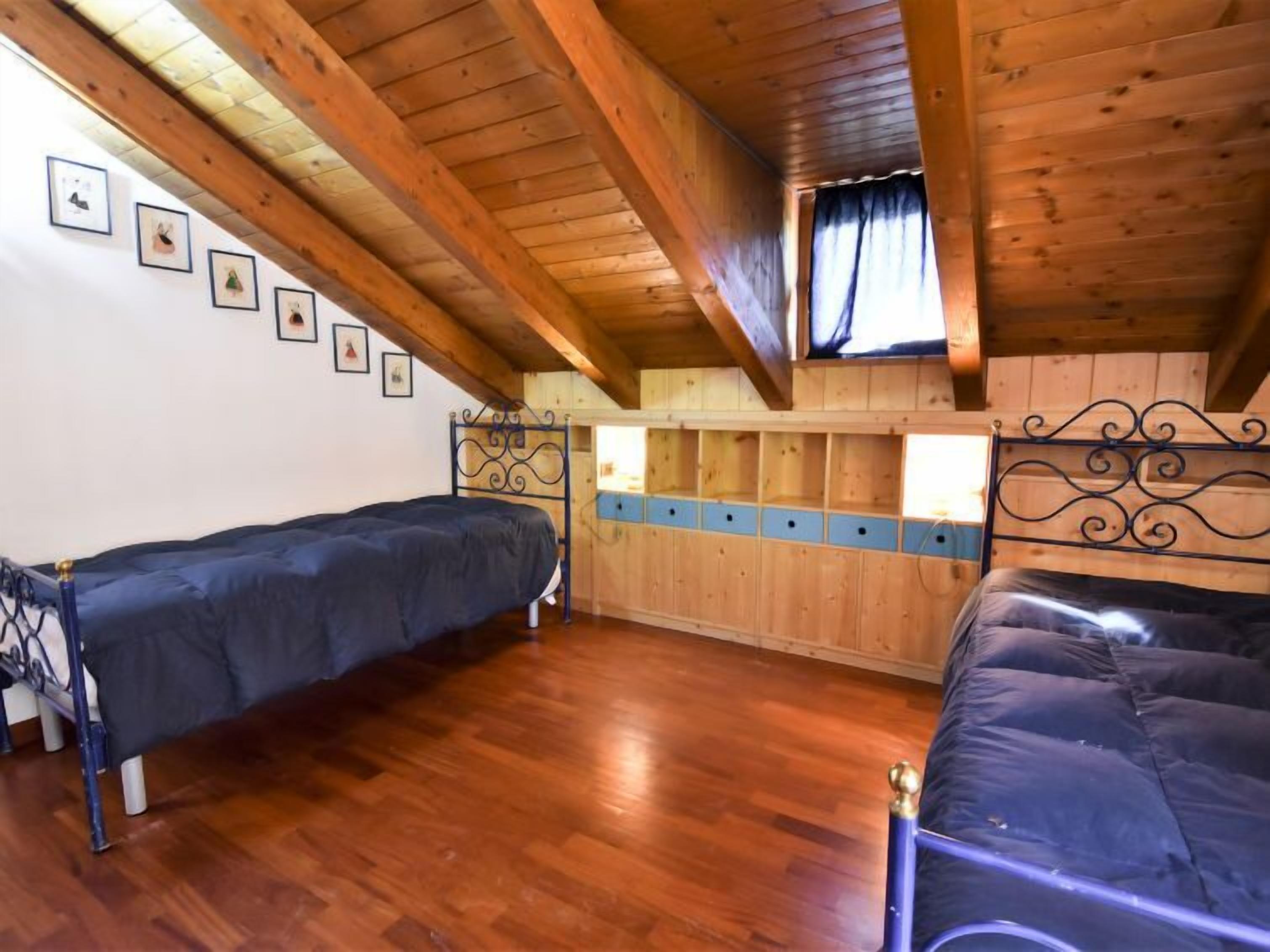A room with two beds, wooden flooring, and a sloped ceiling with exposed beams.