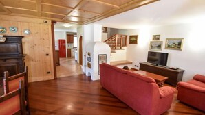 Een woonkamer met een houten vloer, rode banken, een televisie en een keuken op de achtergrond.