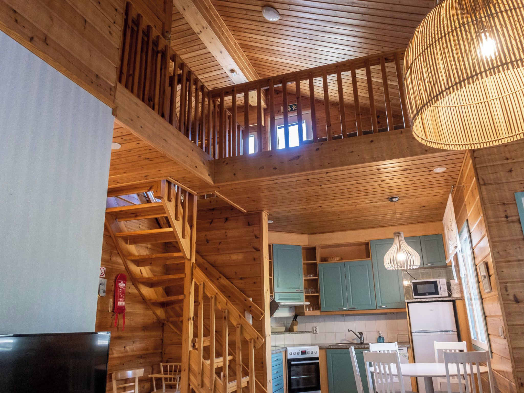 Interior em madeira com escada, cozinha e mesa de jantar.