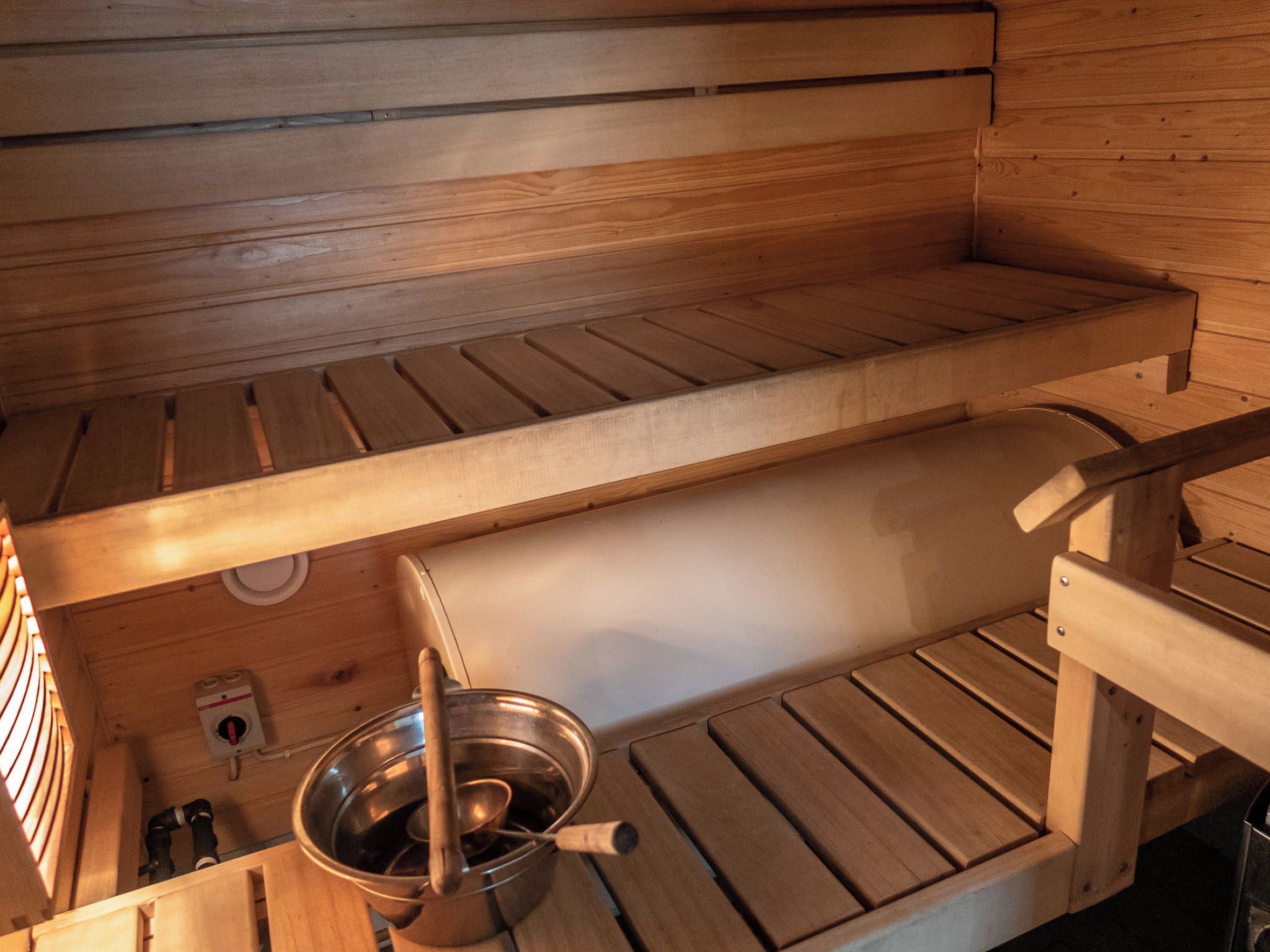 A sauna with wooden benches and a metal basin with a ladle.