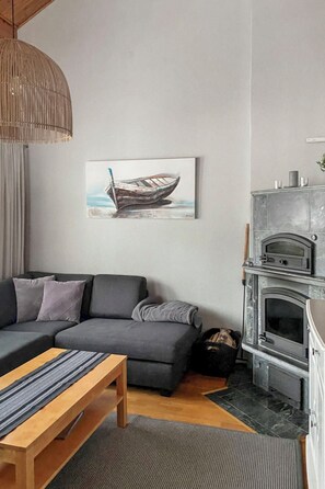 Una sala moderna con un sofá gris, una mesa de centro de madera, una chimenea y un cuadro con un barco.