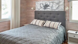 Ein Schlafzimmer mit einer grauen gesteppten Bettdecke, einem grau-gefleekten Kopfteil, zwei gestreiften Kissen, einem großen floralen Kunstwerk über dem Bett und einem weißen Nachttisch mit einer Lampe.