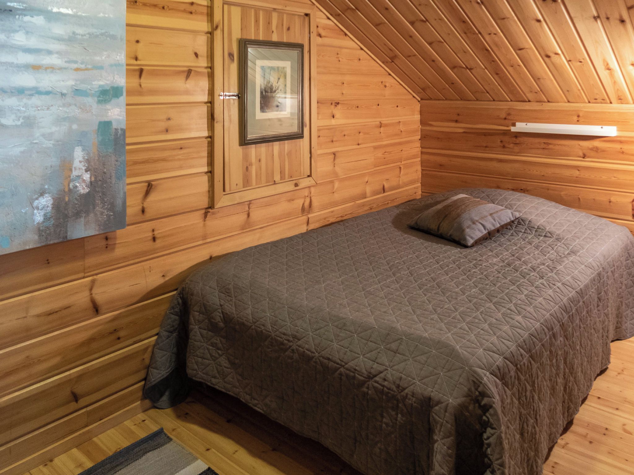 Une pièce de cabane en bois comprenant un lit, un tableau encadré au mur et une fenêtre.