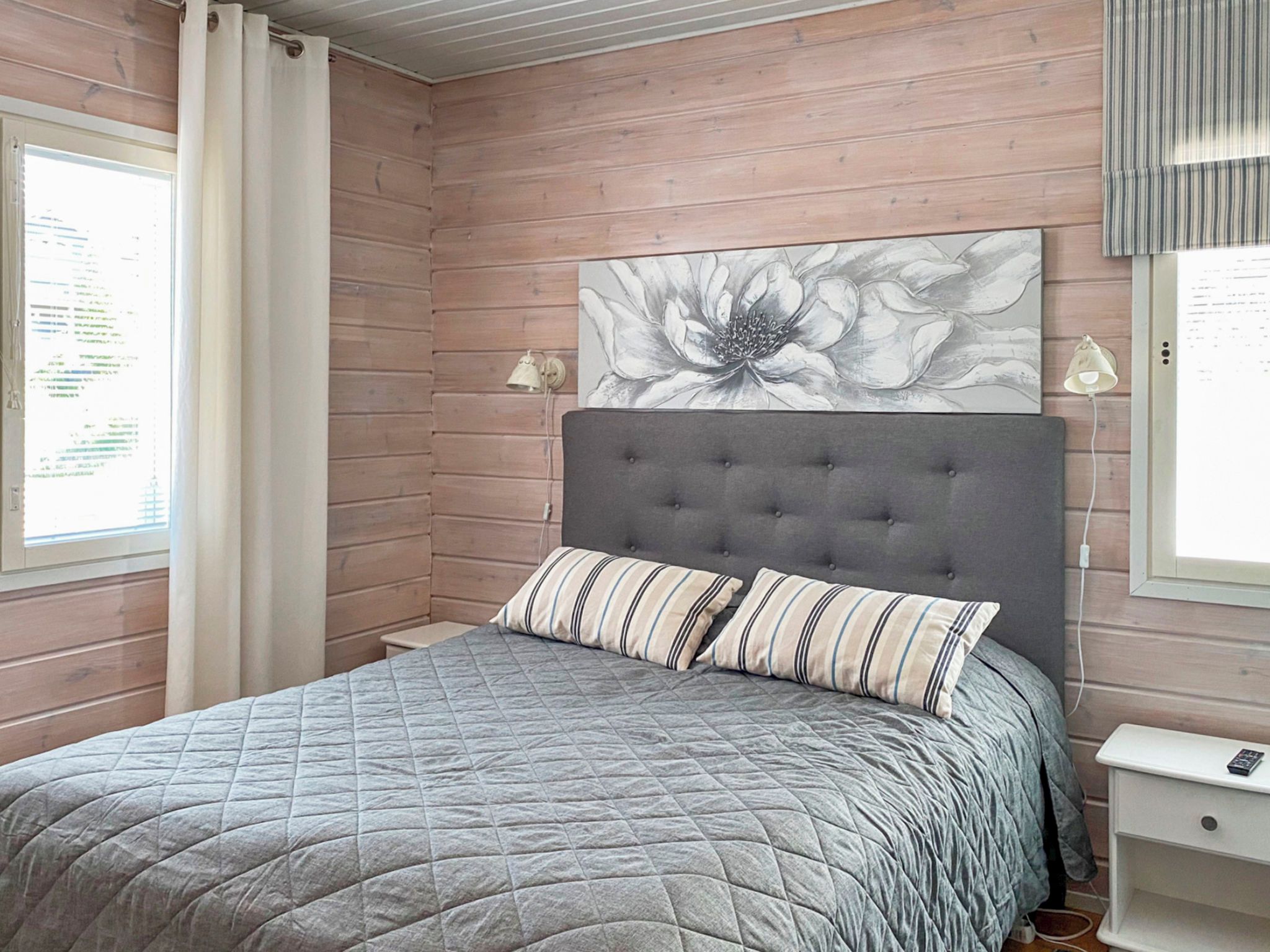 A bedroom with a grey quilted bedspread, a tufted headboard, and a floral artwork above the bed.