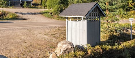 A small wooden shed with a sloped roof, situated on a gravel driveway with a large rock nearby.