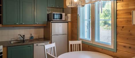 Une cuisine compacte avec des meubles de couleur turquoise, un réfrigérateur blanc, un four à micro-ondes et une table à manger avec des chaises.