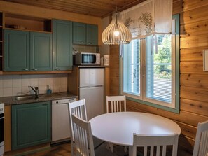 Una cocina compacta con armarios verde azulado, un refrigerador blanco, un microondas y una mesa de comedor con sillas.