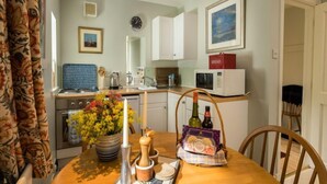 A compact kitchen with white cabinets, a microwave, and a bread box. There's a dining table with a vase of flowers, a candle, and a salt shaker. - Lorn Mill by Interhome (Balloch)